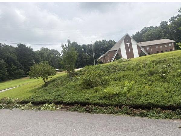 Overgrown roadside hillside below a church before cleanup
