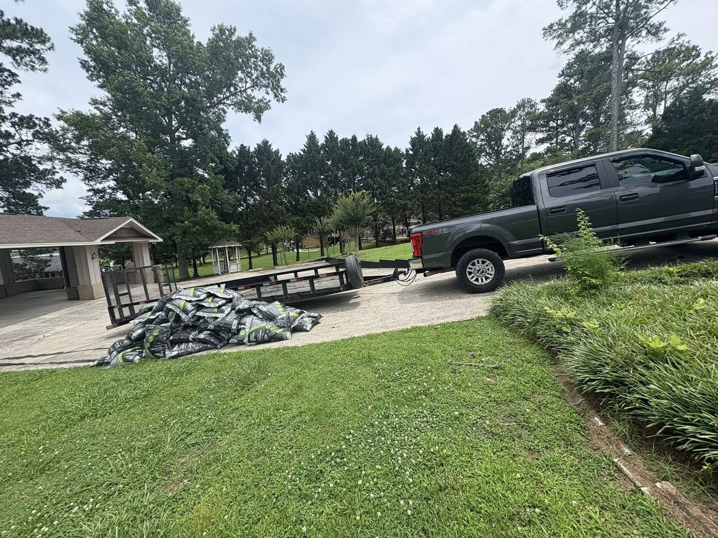 Pickup truck and trailer delivering bagged mulch to a driveway